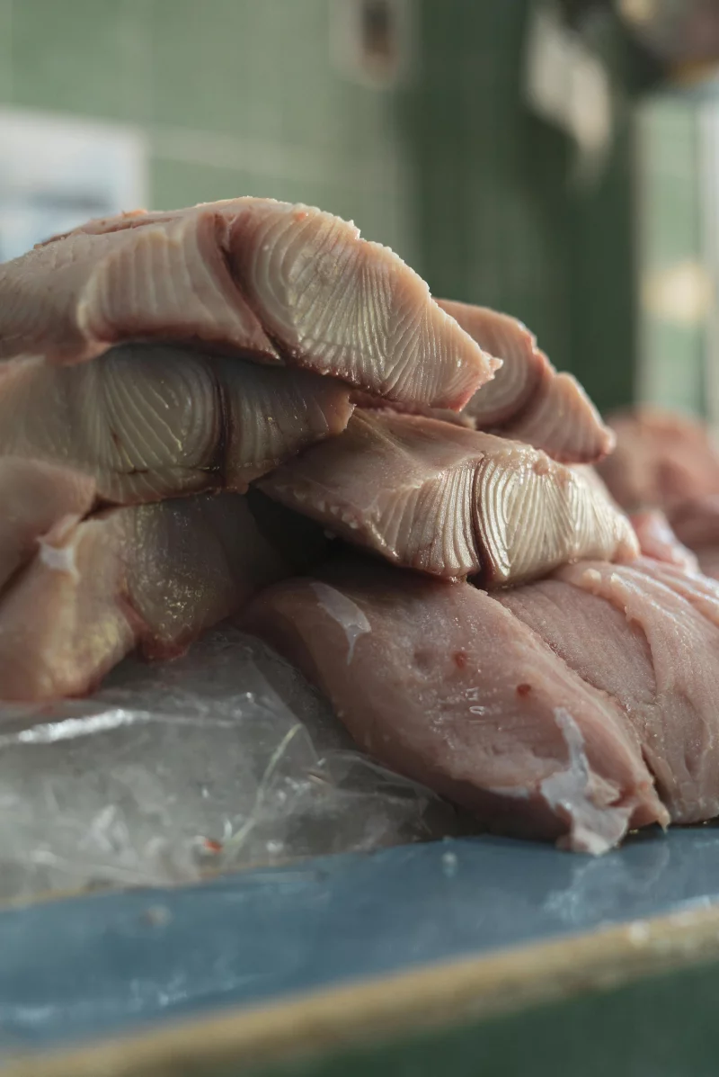 Vertical shot of fresh fish slices stacked on a market counter, displaying texture and freshness.