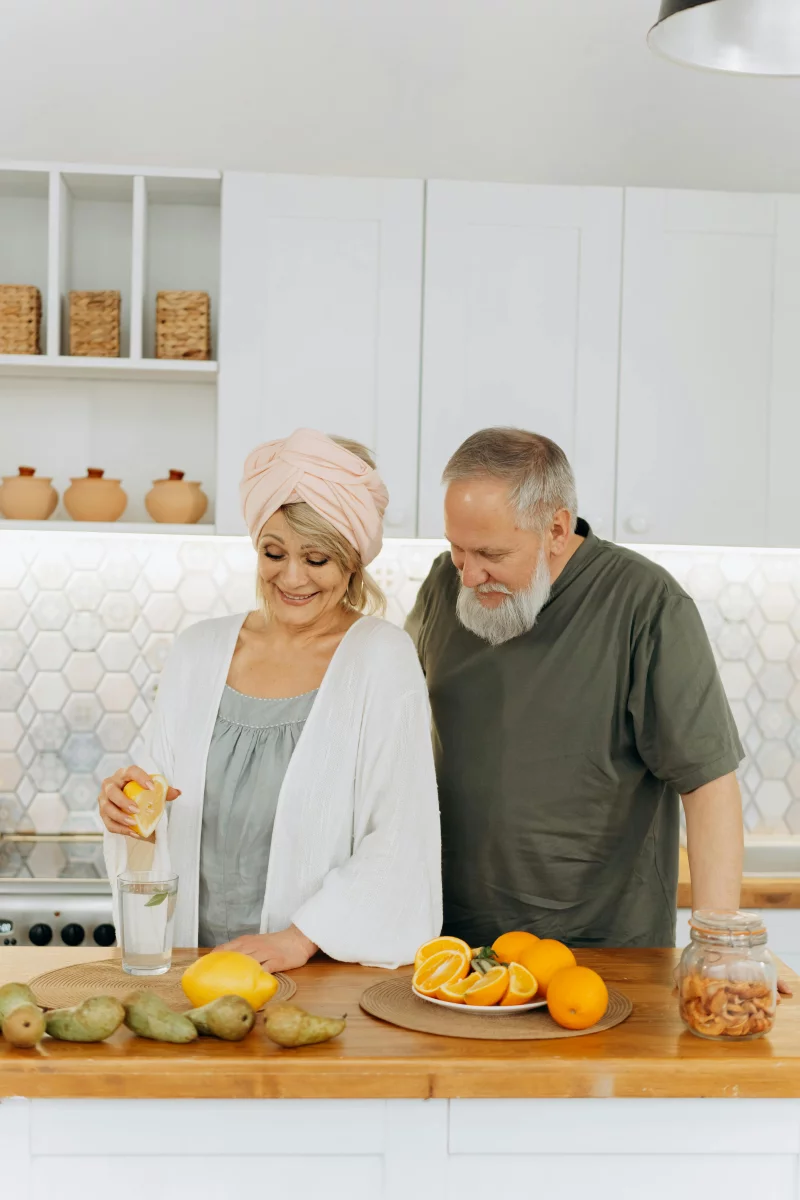 Senior couple smiling while squeezing fresh oranges for juice in a modern kitchen.