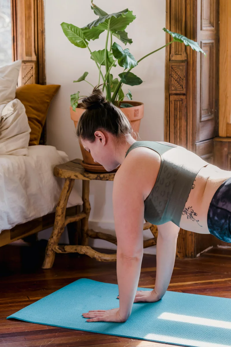 Woman holding a plank yoga pose on a mat at home with natural light in the morning.