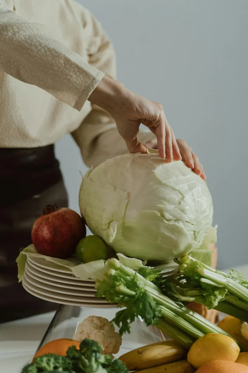 A person arranging cabbage and assorted vegetables on a plate in a kitchen setting.