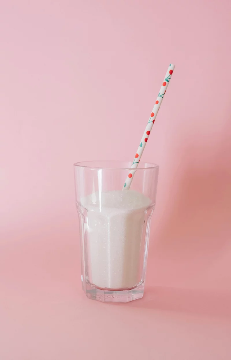 A glass of milk with a decorative straw set against a pastel pink background.