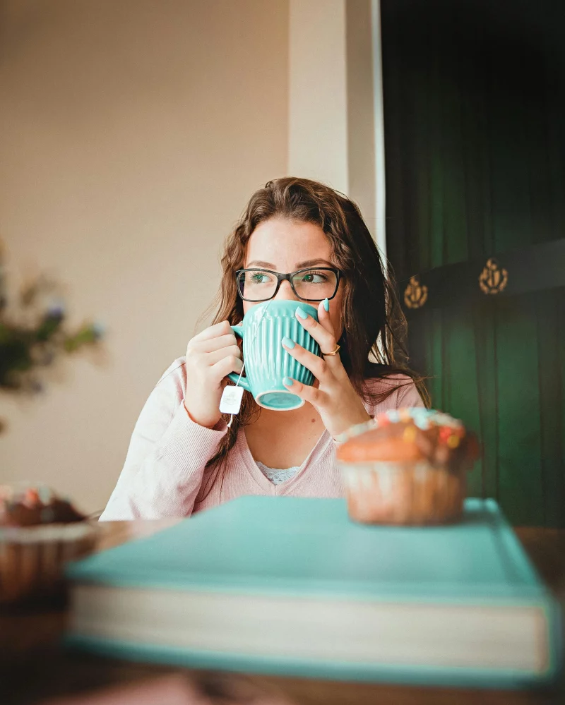 A woman enjoying a morning tea with a pastry in a cozy indoor setting.