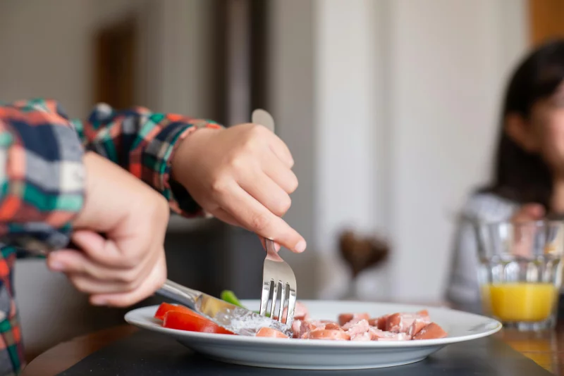 Close-up of hands using fork and knife to slice food on a plate, indoors.