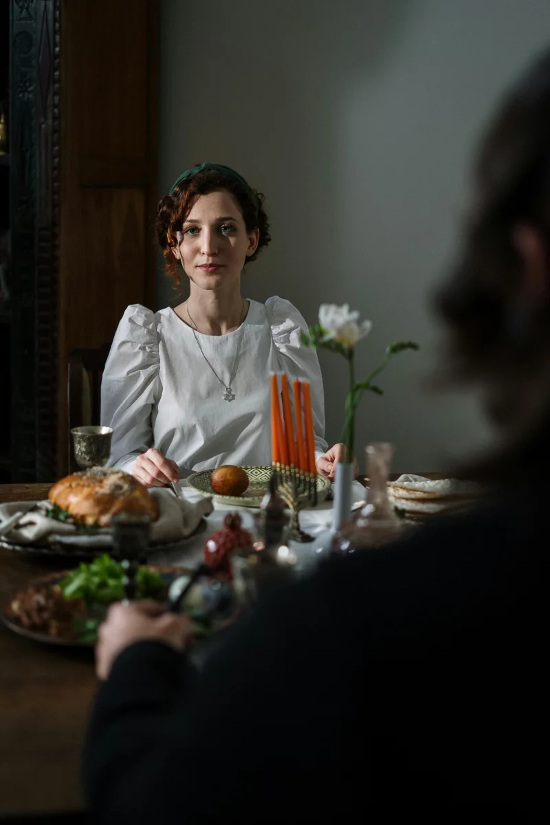 A cozy indoor scene of a Jewish woman enjoying a Shabbat meal with traditional food and candles.