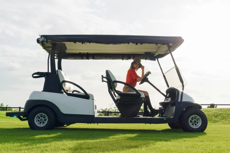 A woman seated on a golf cart at a sunny golf course, enjoying a leisure day outdoors.
