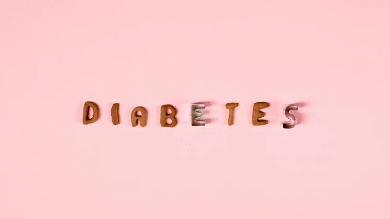 Creative typography of the word 'diabetes' with cookie cutters on a pink background.