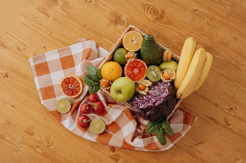 A vibrant flat lay of assorted fresh fruits on a checkered cloth over a wooden surface, perfect for healthy lifestyle concepts.