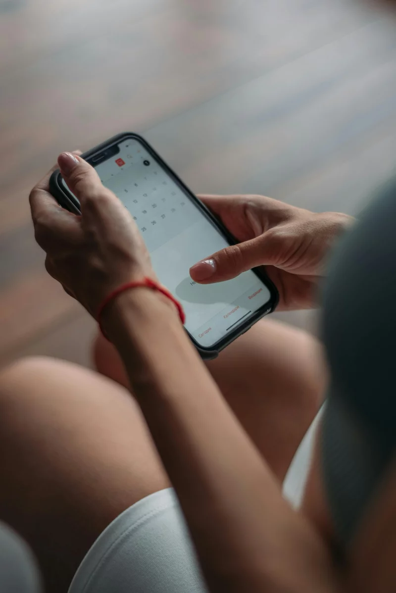 Close-up of a person using a smartphone to access the calendar app indoors.