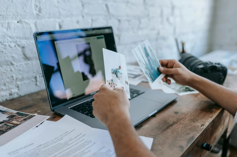 A person reviews photographs on a desk with a laptop, in a modern workspace.