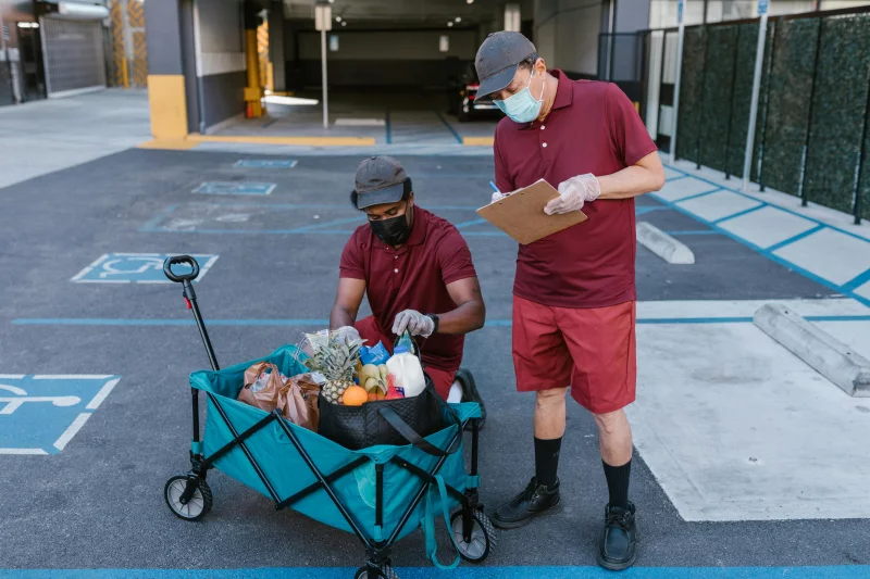Two masked delivery workers handling groceries in an outdoor setting.