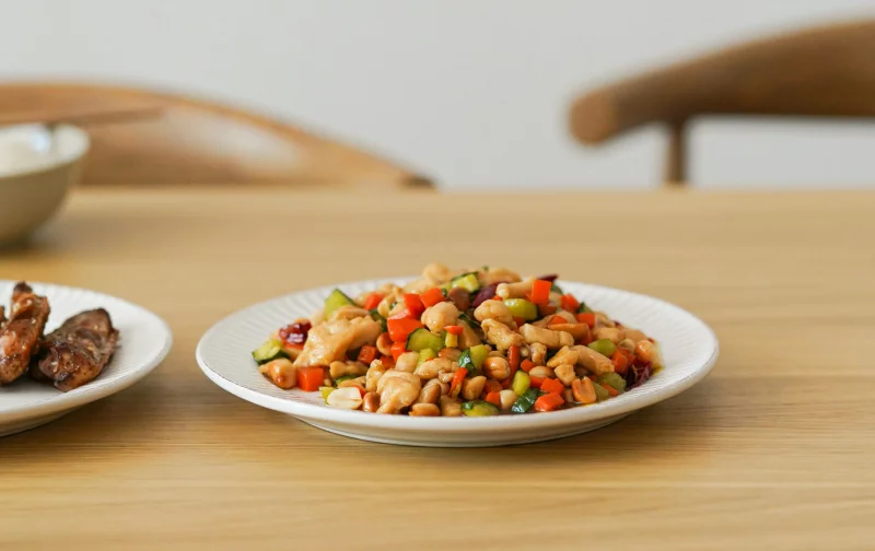 Close-up of a healthy, colorful stir fry with vegetables and protein on a white plate indoors.