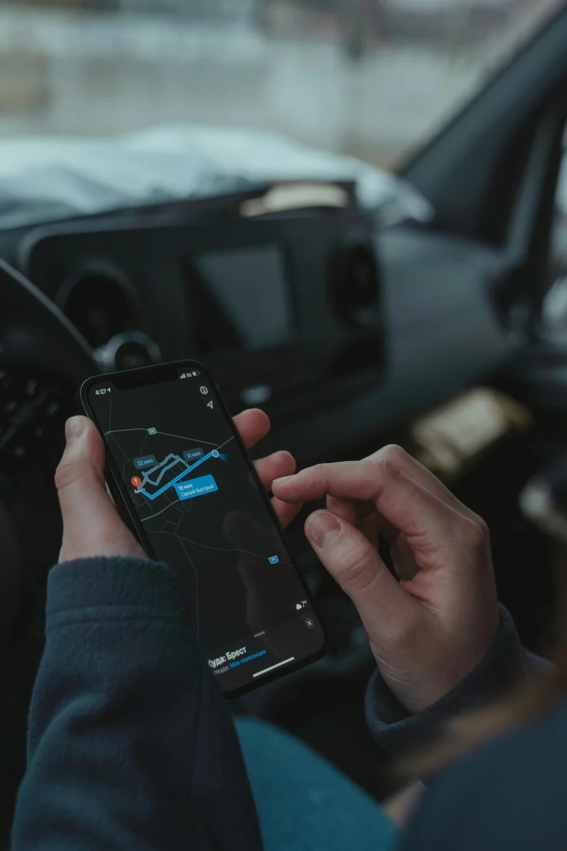 Close-up of a person using a smartphone for GPS navigation inside a car, showing the screen with a route.