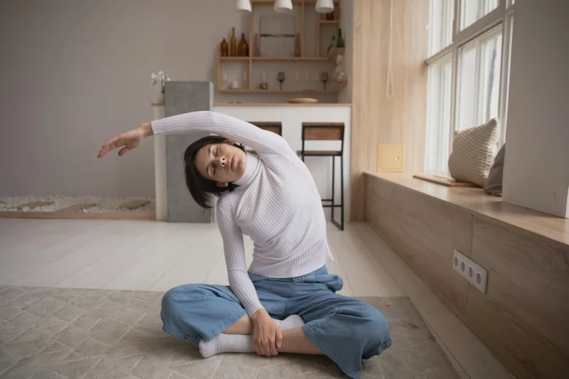 Woman performing a side stretch yoga pose indoors, emphasizing relaxation and fitness in a cozy setting.