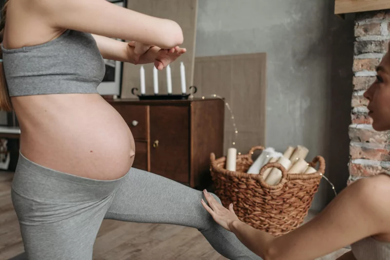 Pregnant woman doing yoga indoors with instructor assistance, emphasizing fitness and well-being.