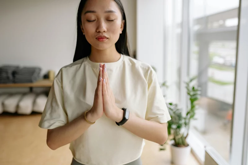 Young woman practicing meditation indoors, symbolizing peace and relaxation with eyes closed.