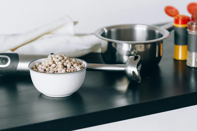 Bowl of chickpeas with cooking tools and spices on kitchen counter.