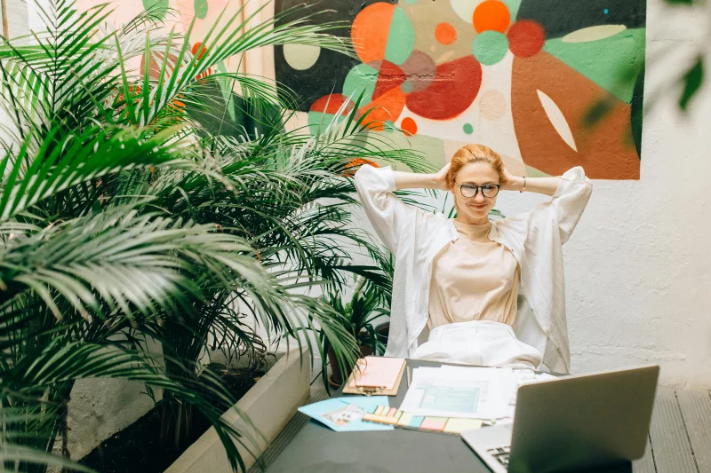 A relaxed woman sits with a laptop amidst lush indoor plants, creating a serene workspace.