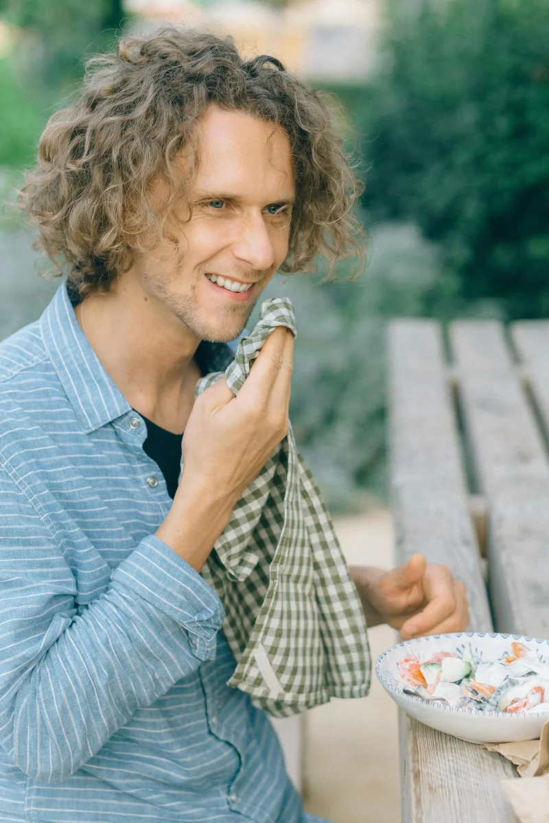 A young man enjoys a fresh salad at an outdoor picnic table, embodying healthy eating.