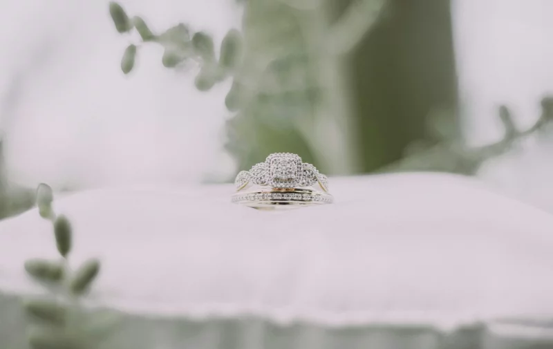 Close-up of a diamond wedding ring on a white cushion surrounded by greenery. Perfect for bridal themes.