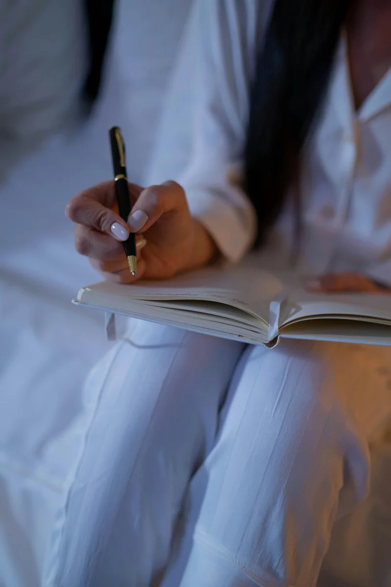 A person in pajamas writes notes in a notebook with a pen, capturing thoughts before bed.