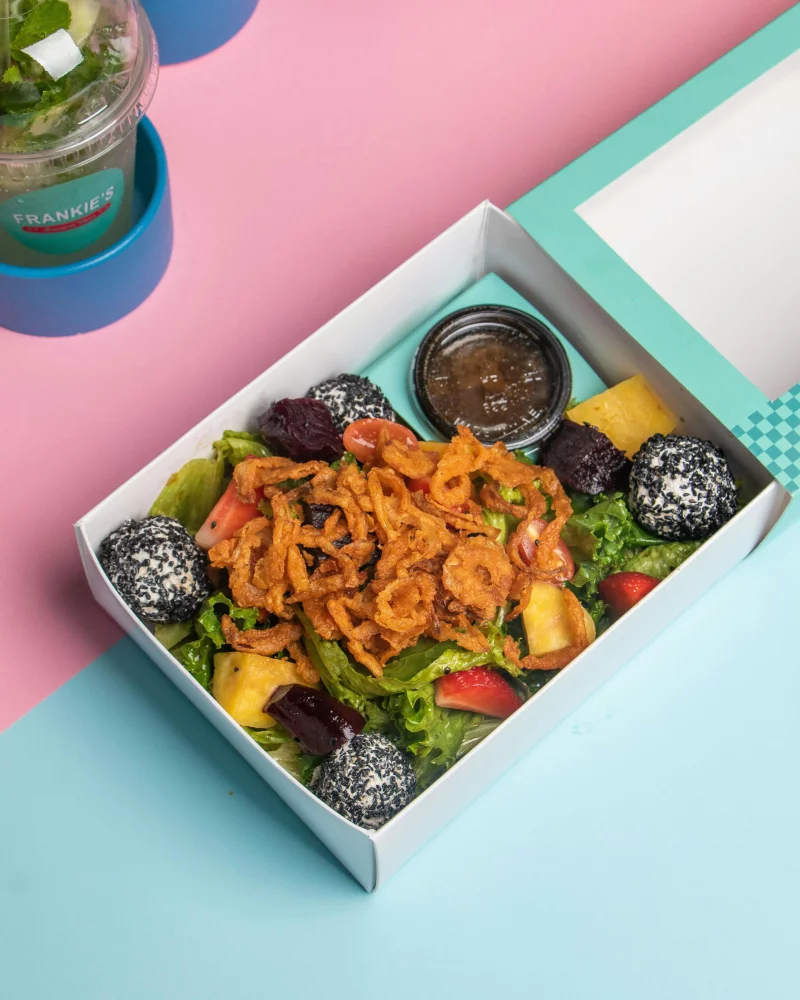 Delicious mixed salad with fresh fruits and crispy toppings in a takeaway box.