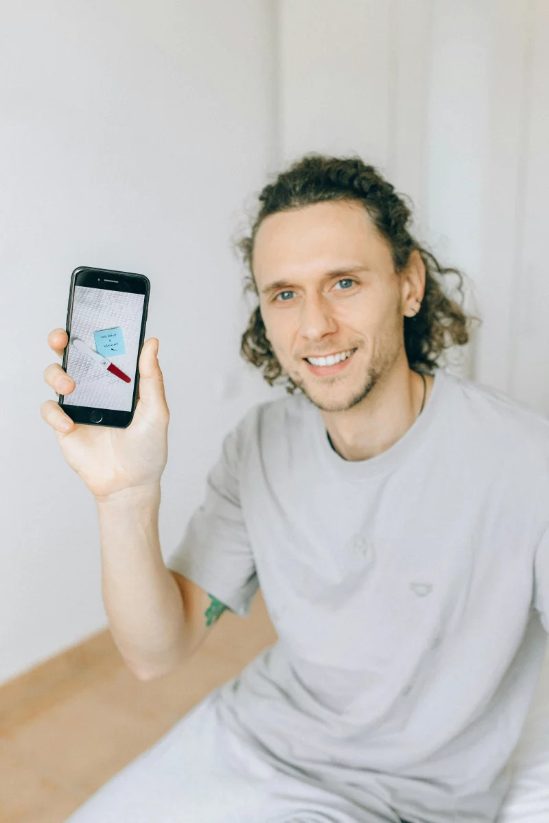 Man smiling while holding a smartphone displaying a note app, indoors.
