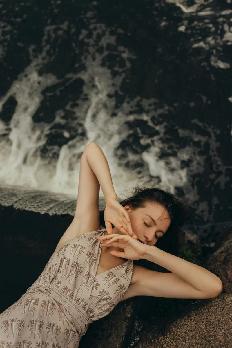 A serene woman lying near a waterfall with eyes closed, embodying tranquility and nature.