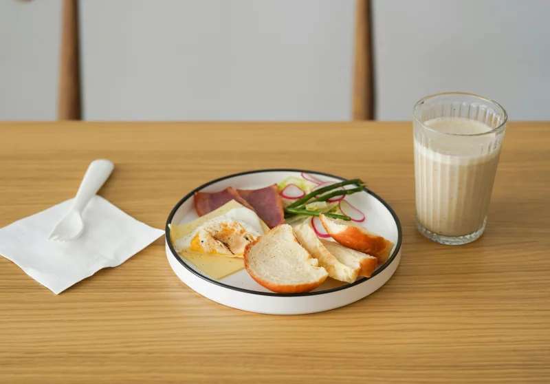 Healthy breakfast with bread, cheese, deli meat, and smoothie on a wooden table.