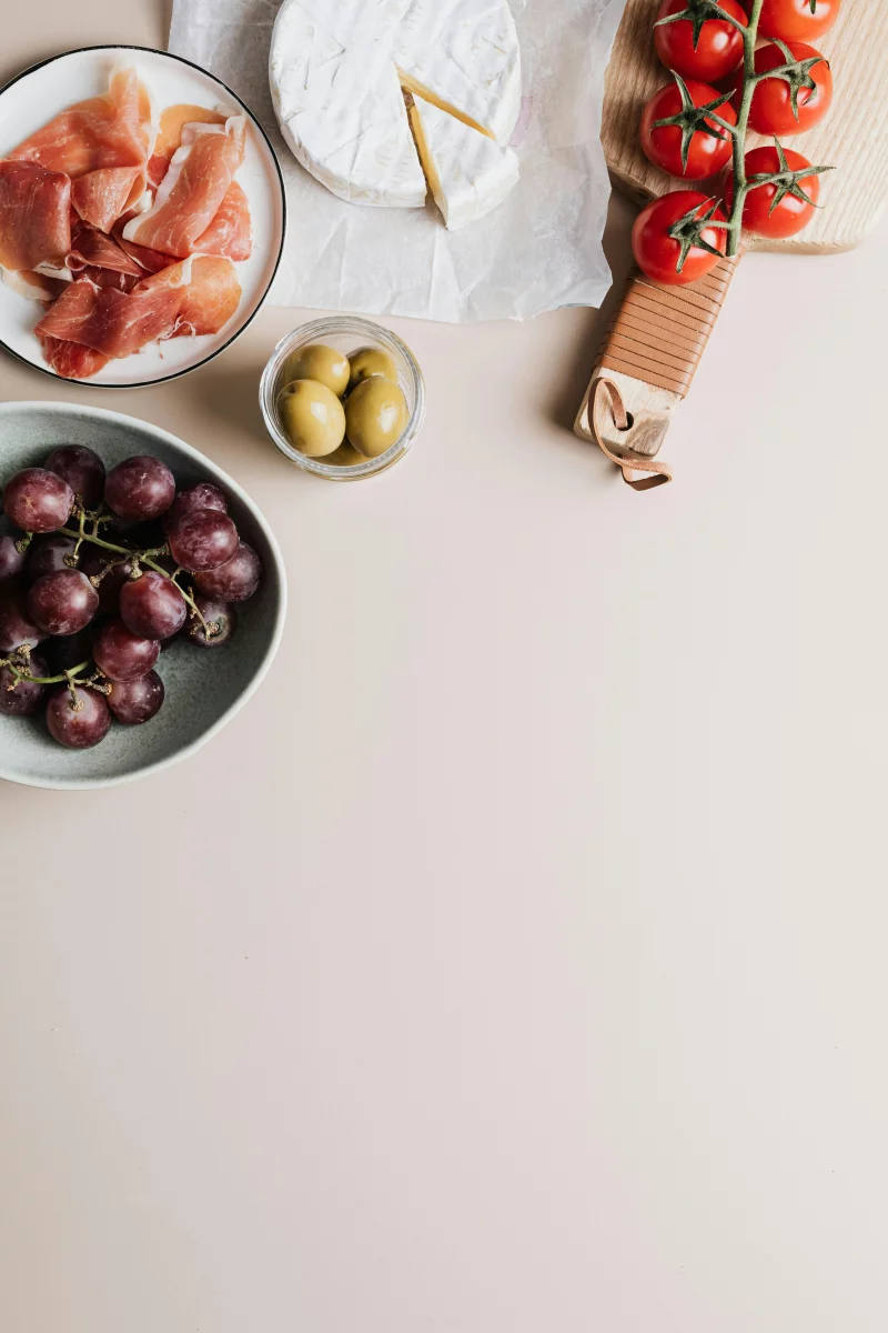 Gourmet platter with camembert, prosciutto, tomatoes, grapes, and olives on a table with ample copy space.