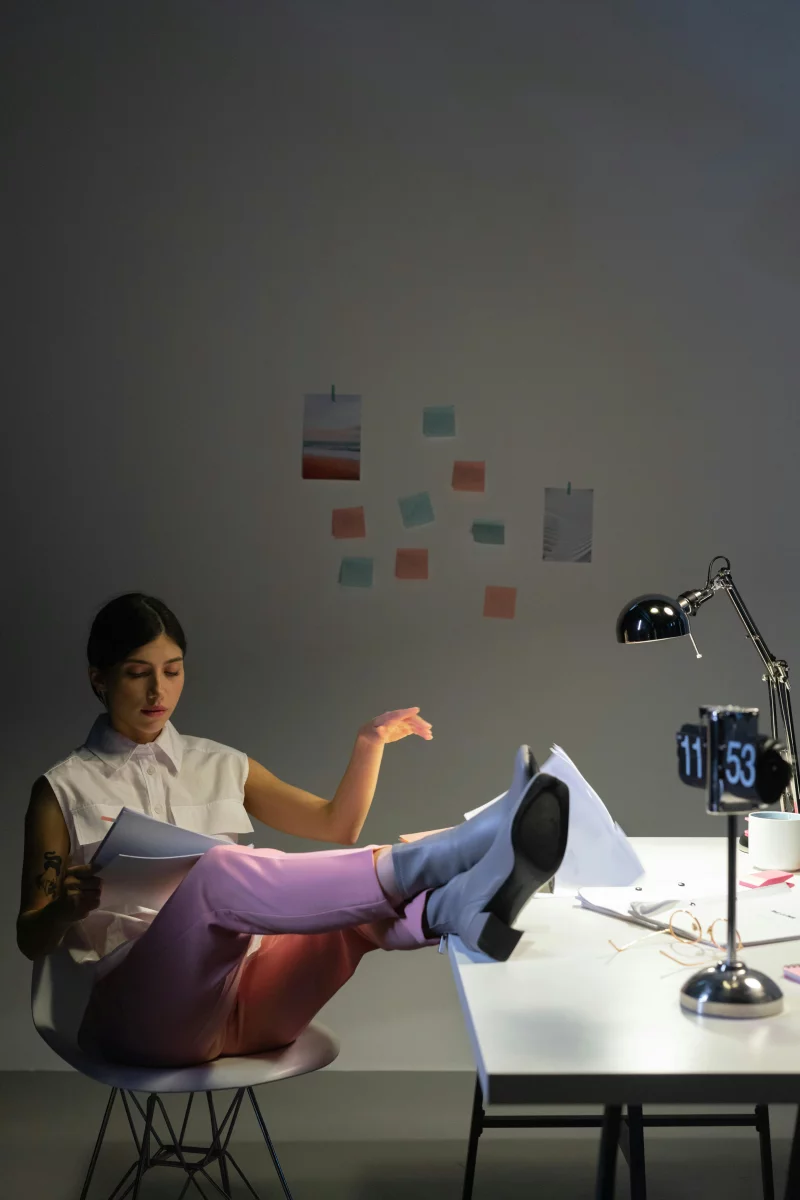 A woman in an office setting, reading documents with legs casually on the table.