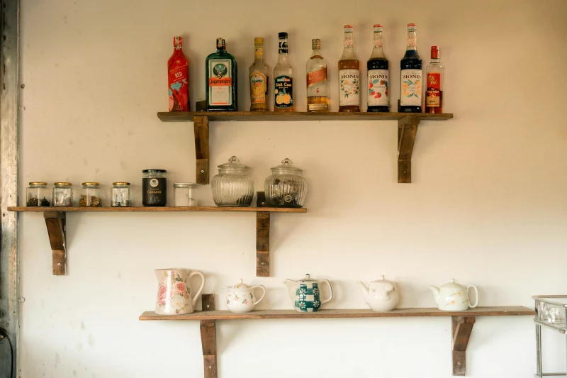 Wooden shelves with alcohol bottles and teapots in a cozy kitchen setting.