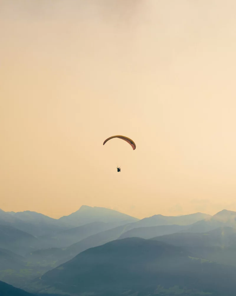 A paraglider soars gracefully over the misty, layered mountains at sunset, capturing serene adventure.