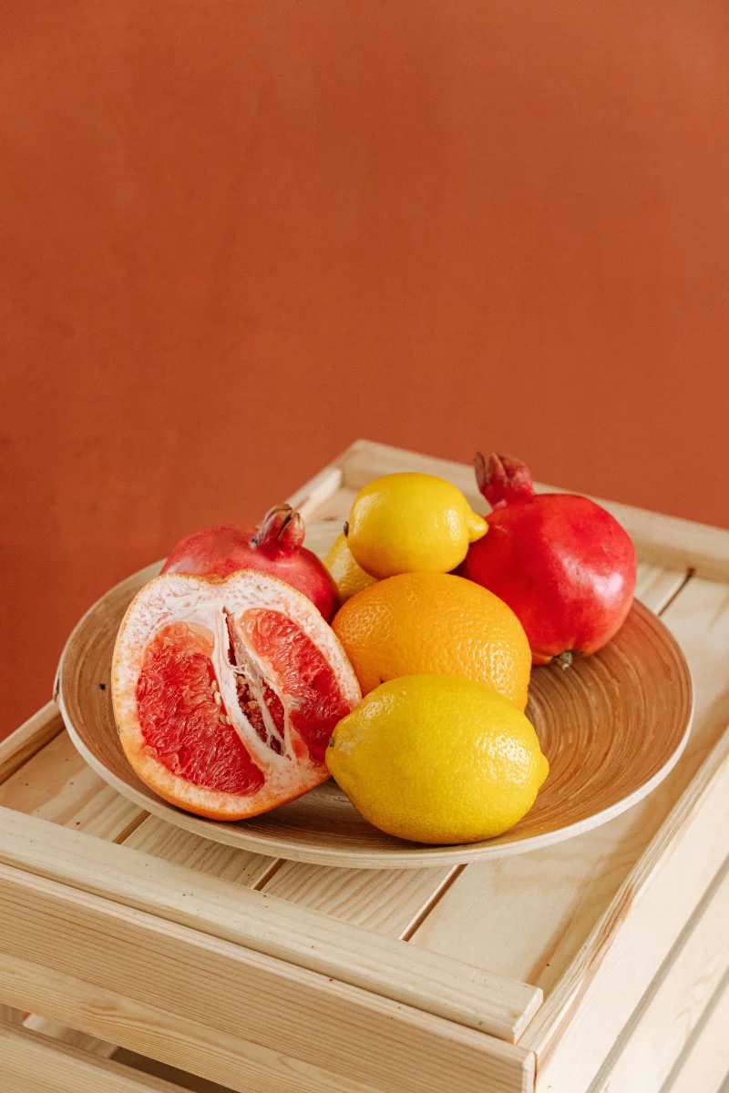 Colorful fruit arrangement with citrus and pomegranates on wooden crate.