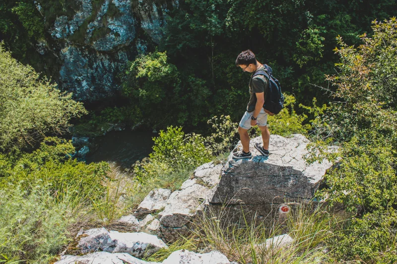 Man stands on cliff edge, enjoying a sunny day in nature.