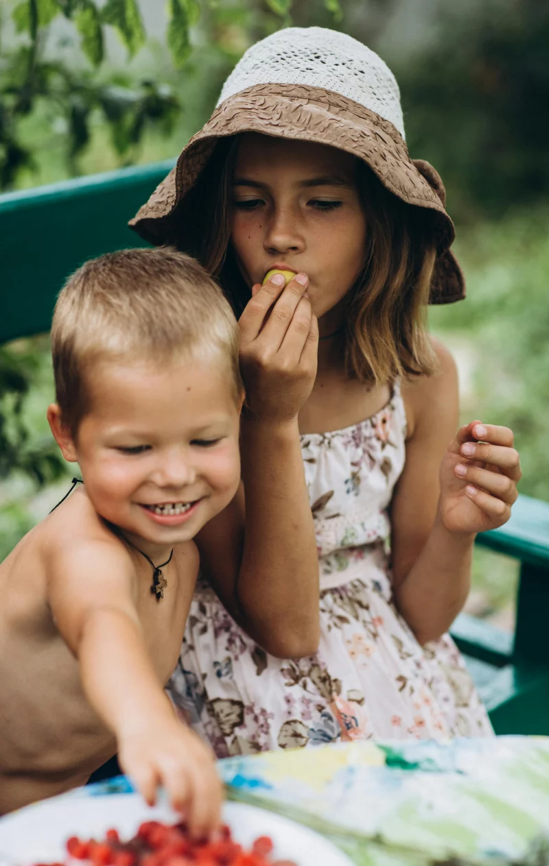 Two kids happily eating fresh berries outdoors on a summer day.