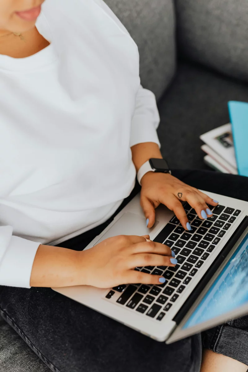 Close-up view of a person typing on a laptop while sitting on a couch, perfect for remote work concepts.