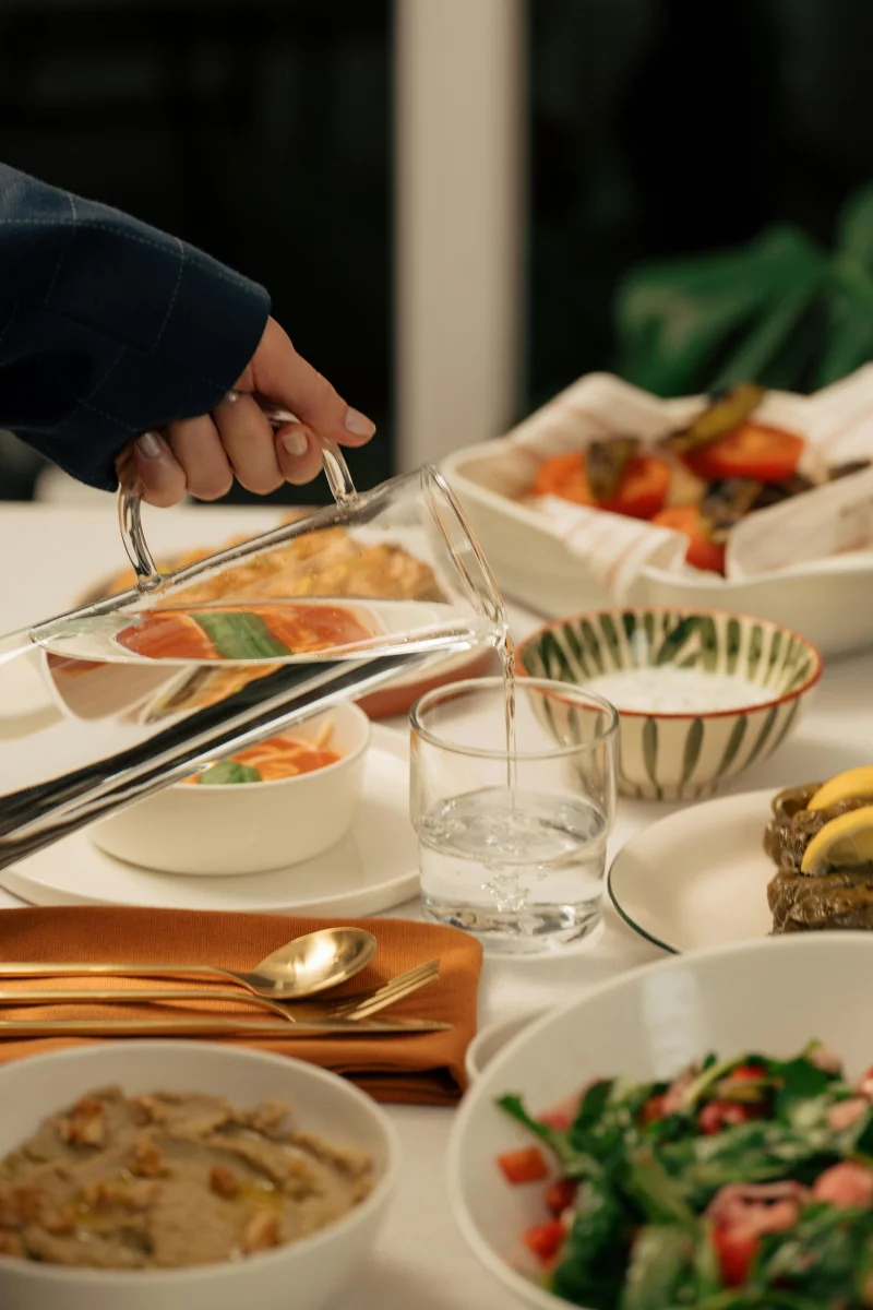 A beautifully arranged dinner table with assorted dishes and a hand pouring water into a glass.
