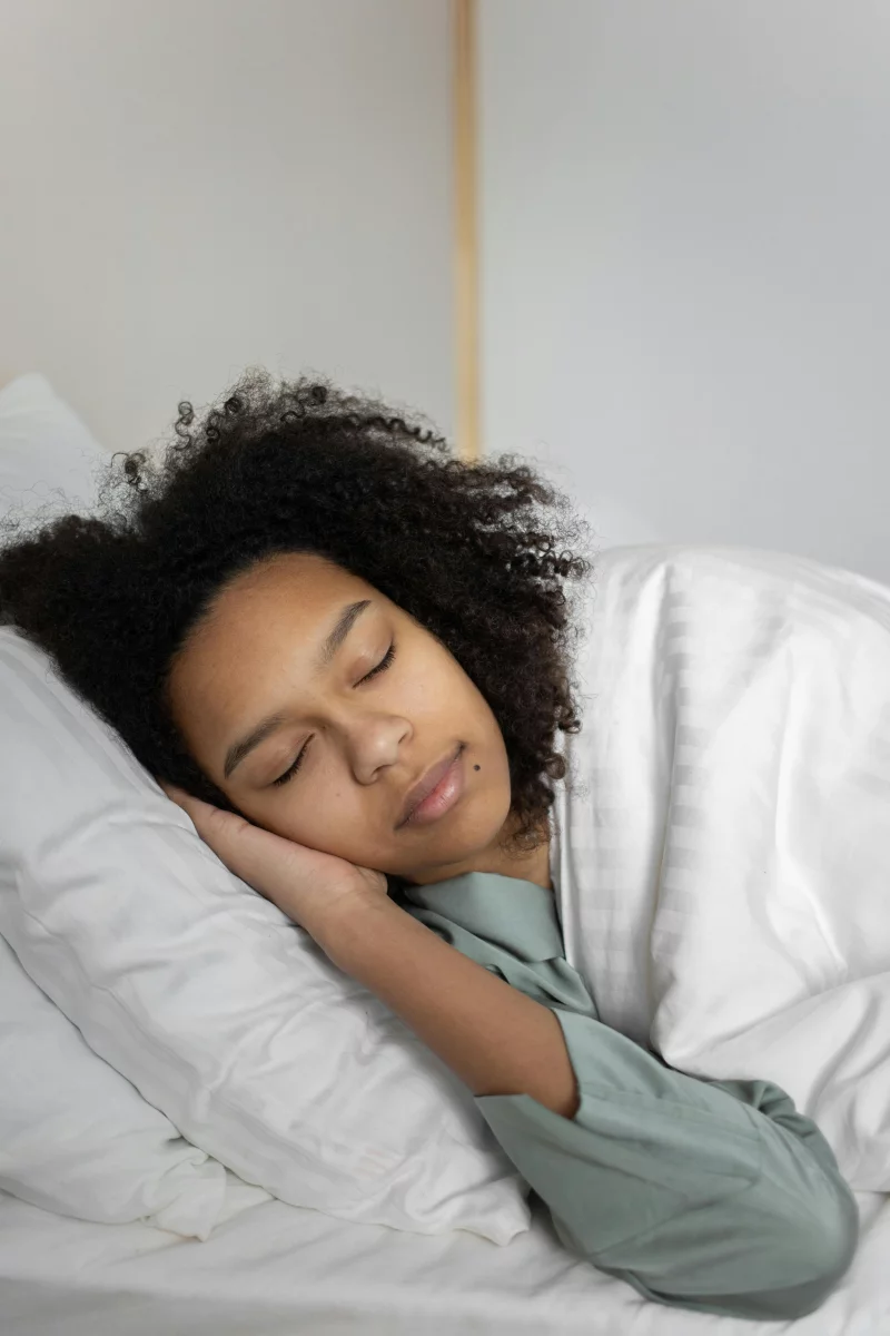 Relaxed woman with curly hair sleeping peacefully in a cozy bed.