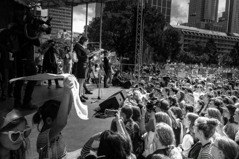 A large crowd at an outdoor gathering in Sydney, featuring a public speaker on stage.
