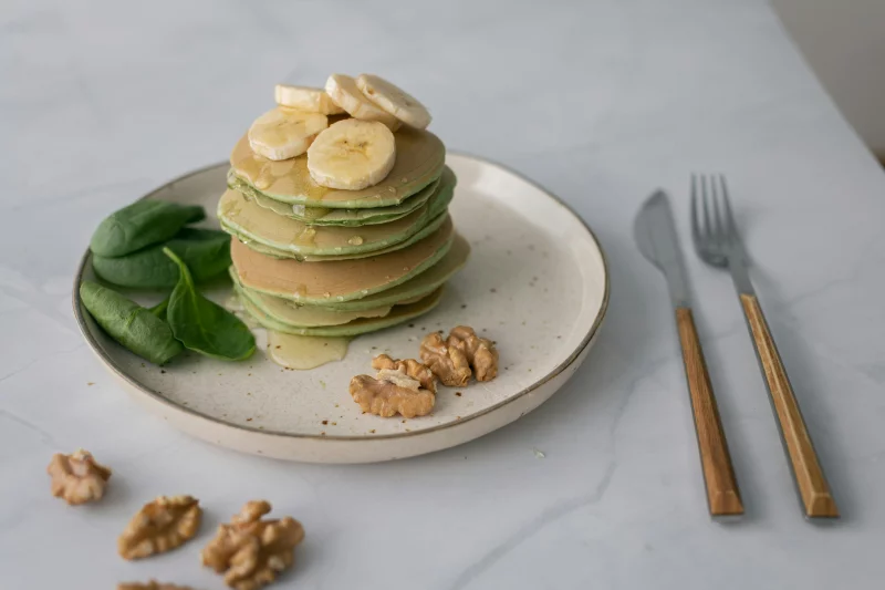 Delicious stack of banana spinach pancakes garnished with walnuts and honey.