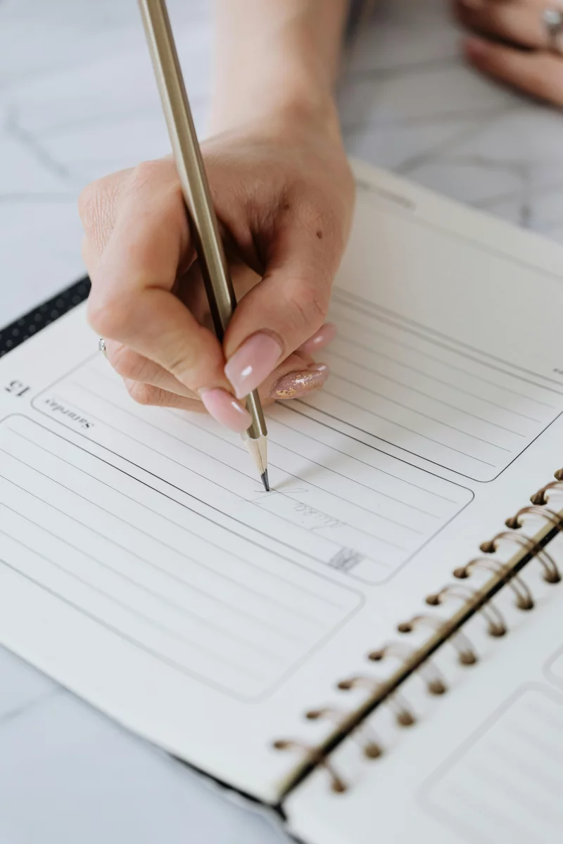 A close-up of a hand writing in a planner with a pencil. Ideal for organization themes.