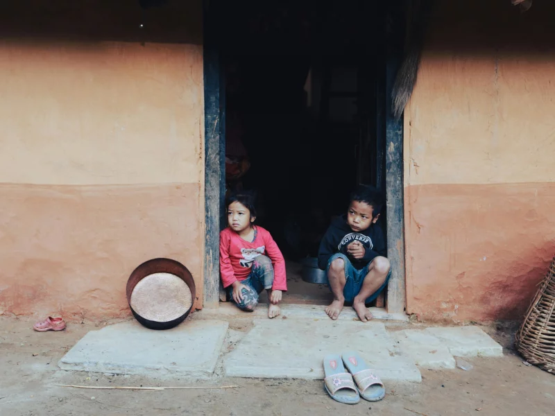 Two children sitting outside the doorway of a rural home, reflecting a quiet moment.