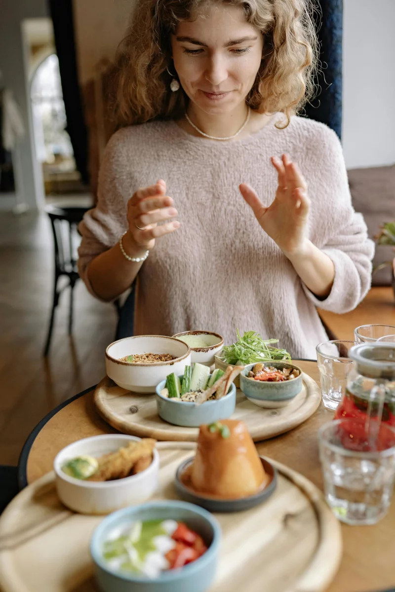 A woman in a sweater enjoying a variety of small dishes at a dining table indoors.