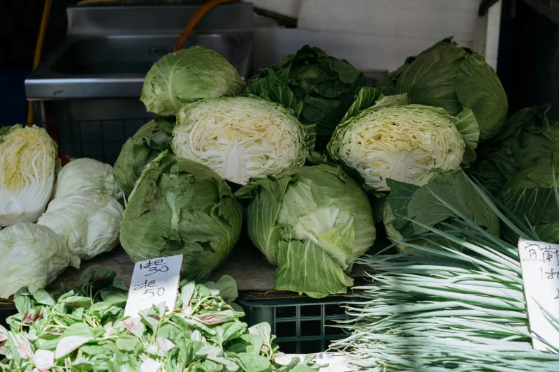 Close-up view of fresh cabbage and greens displayed at an outdoor market stall.