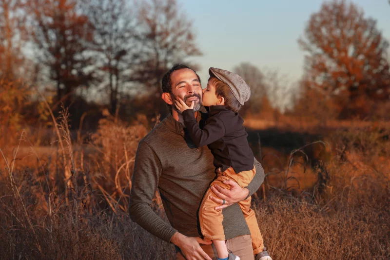 Father holding his son outdoors during a warm autumn sunset, displaying love and connection.