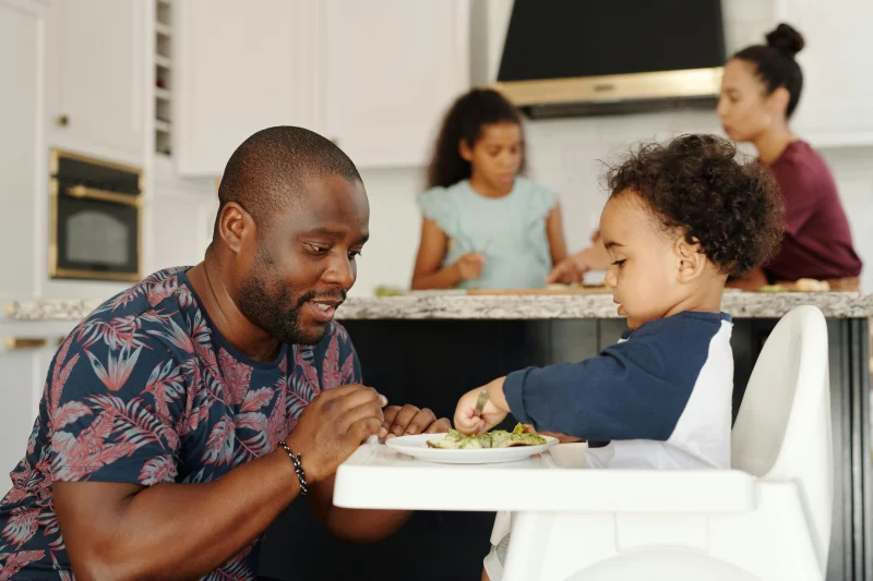 Father feeds child in a lively family setting, capturing warmth and connection.