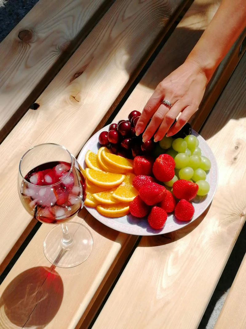 A refreshing plate of fruit with a hand reaching over, paired with a chilled drink on a picnic table.