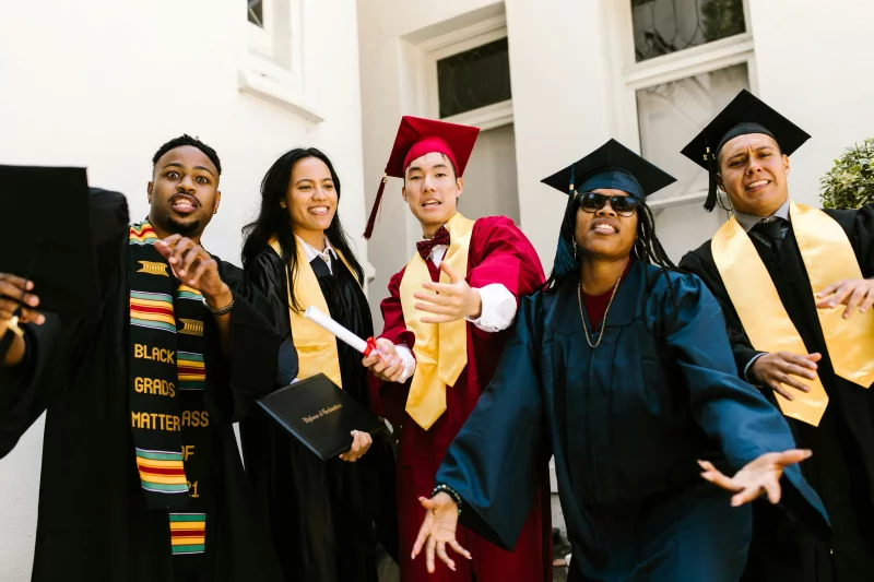 Joyful graduates in academic gowns celebrate their achievement outdoors.