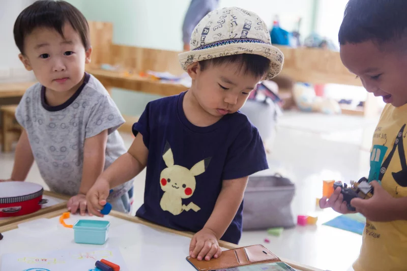 Three young children playing creatively indoors with toys and art supplies.