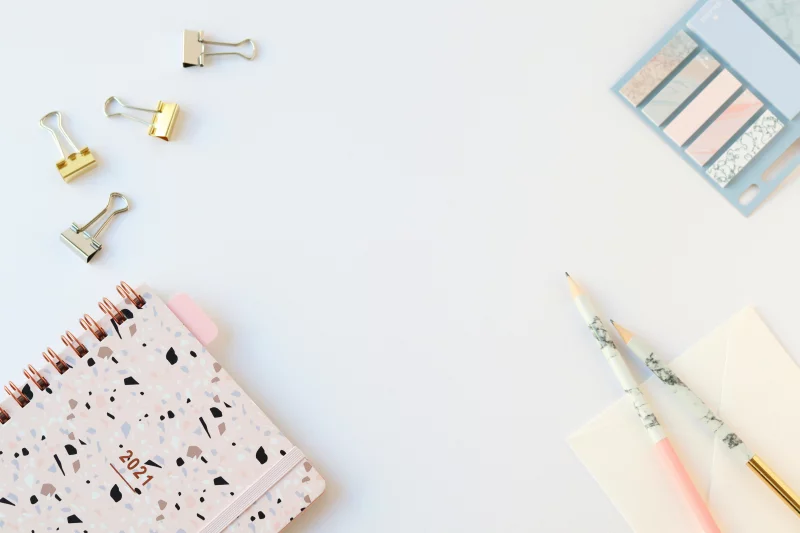 Flat lay of a stylish 2021 planner and stationery on a white desk, perfect for planning and organization.